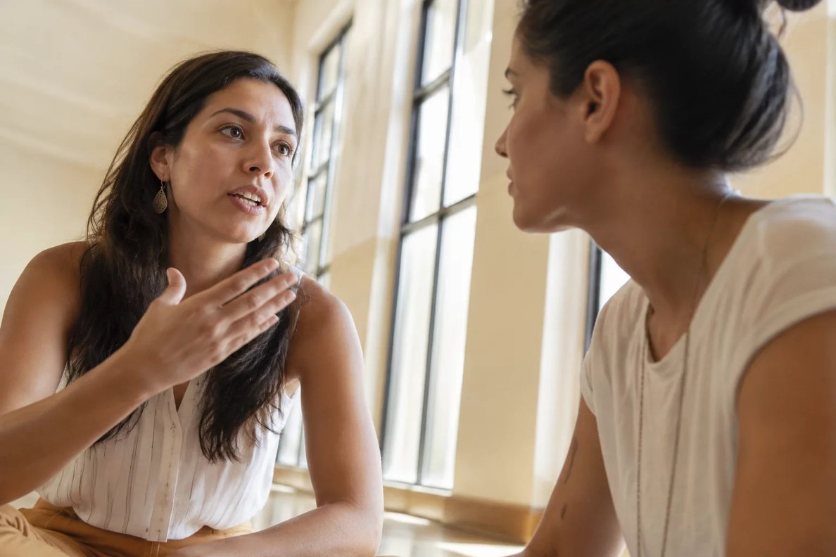 Duas pessoas sentadas de frente uma para a outra à mesa: uma fala, a outra registra por escrito